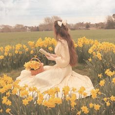 a woman sitting in the middle of a field with yellow flowers and holding a book