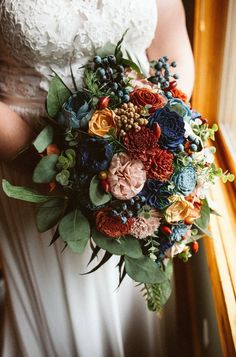 a bride holding a bouquet of flowers and greenery on her wedding day in front of a window