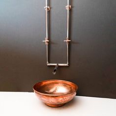 a copper bowl sitting on top of a white counter next to a metal wall hook