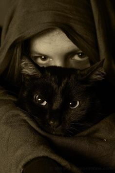 a black cat laying on top of a woman's chest under a hooded hood