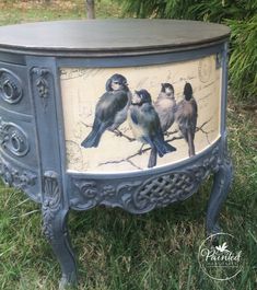 a painted cabinet with birds on it sitting in the grass next to some bushes and trees