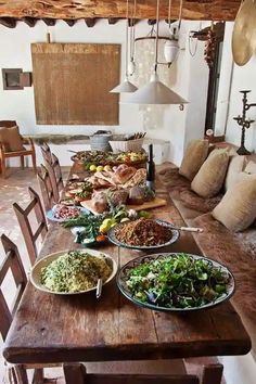 a wooden table topped with lots of food on top of a dining room table next to a couch