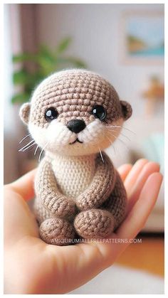 a small crocheted otter is sitting on someone's hand and looks at the camera