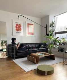 a woman sitting on a black couch in a living room next to a table and potted plant