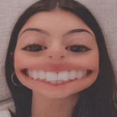 a woman with long black hair and big hoop earrings smiles at the camera while wearing a fake smile on her face