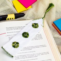 an open book with green buttons on it next to some markers and pencils in the background