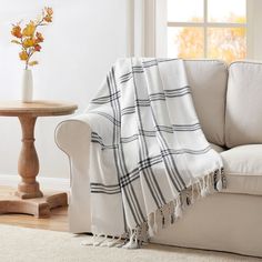 a white couch with a plaid blanket on it next to a small table and window