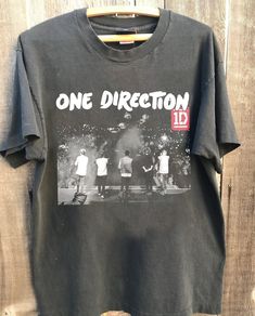 one direction t - shirt hanging up on a wooden wall with the words, one direction