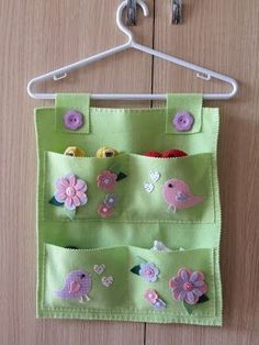 a green bag hanging on a white hanger with buttons and flowers in the pocket