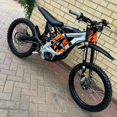 an orange and black dirt bike parked next to a brick wall