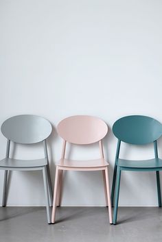 three different colored chairs against a white wall