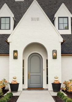 a white house with two black planters and pumpkins on the front door area