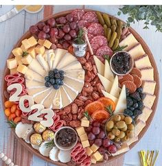 a platter filled with different types of cheeses and fruit on top of a wooden table