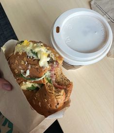 a person holding a sandwich in their hand with a cup on the table next to it