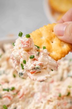 a cracker with crab salad in it is being held up over a bowl of dip