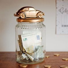 a glass jar filled with money sitting on top of a wooden table next to gold coins