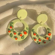 a pair of earrings with oranges painted on the inside of them, sitting on a white surface