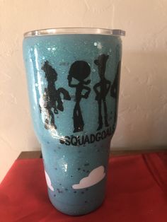 a blue cup with black silhouettes on it sitting on top of a red table