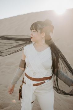 a woman with long black hair and white clothes in the desert, holding her scarf over her head