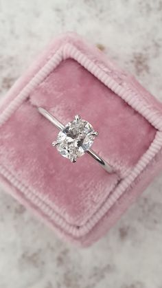 an engagement ring sitting on top of a pink velvet box with a diamond in it