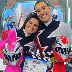 a man and woman posing for a photo in front of a movie clapper with power rangers behind them