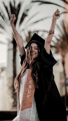 a woman wearing a graduation cap and gown with her arms in the air