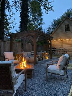 an outdoor fire pit surrounded by chairs and tables with lights on the side of it