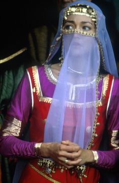 a woman in a purple and red outfit with veil on her head is looking off to the side