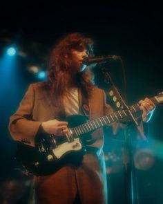 a man with long red hair playing an electric guitar in front of a microphone on stage