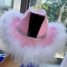 a pink hat with white feathers and a cell phone in it's centerpiece