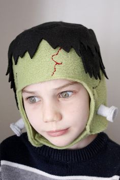 a young boy wearing a green knitted hat with black hair and red stitches on it