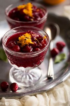 two small glasses filled with cranberry sauce on a silver tray next to oranges