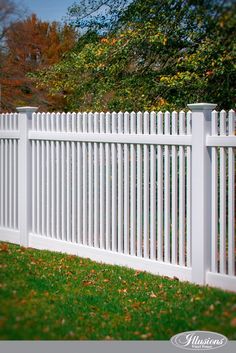 a white picket fence with green grass and trees in the background