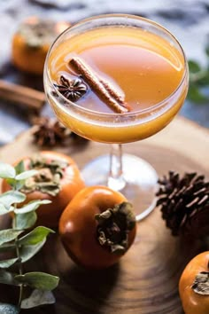 a glass filled with liquid sitting on top of a wooden tray next to oranges and pine cones