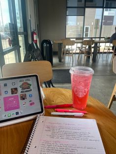 a table with a notebook, pen and cup on it next to a tablet computer