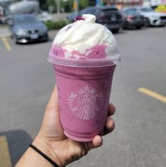 a hand holding up a pink drink with whipped cream on top in the middle of a parking lot