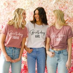 three women standing next to each other in front of a flower wall wearing matching tshirts