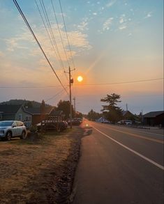 the sun is setting over an empty street with cars parked on the side of the road