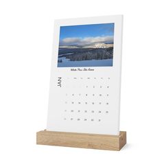 a desk calendar on a wooden stand with a mountain scene in the background and blue sky