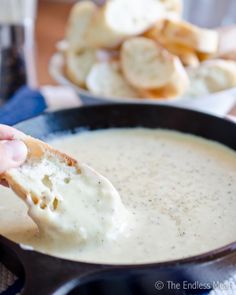 a person dipping some bread into a bowl of cream cheese soup with crackers in the background