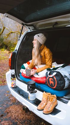 Woman sitting on the back of her SUV in a sleeping bag with coffee in her hands. Linked to a blog post that talks about how to sleep in your SUV on road trips. Winter Camping Gear, Car On Road, Car Camping Essentials, Sleeping In Your Car, Camping Essentials List, Suv Camping, Road Trip Camping, How To Sleep, Backcountry Camping