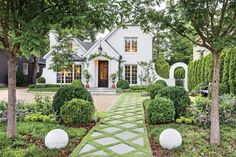 a white house with lots of trees and bushes around the front yard, surrounded by greenery