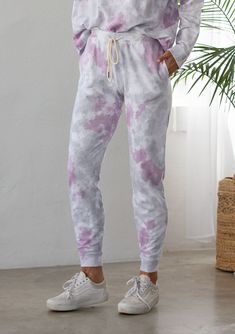 [Color: Lavender Combo] A woman standing outside wearing a classic cotton jogger pant in a splatter tie dye wash. Featuring a drawstring waistband Acid Wash Bottoms With Elastic Waistband For Loungewear, Trendy Tie Dye Bottoms For Loungewear, Tie Dye Pants With Elastic Waistband For Loungewear, Trendy Tie Dye Loungewear Bottoms, Casual Purple Joggers For Loungewear, Casual Purple Sweatpants For Loungewear, Casual Tie Dye Sweatpants Relaxed Fit, Casual Tie-dye Sweatpants With Relaxed Fit, Casual Relaxed Fit Tie-dye Sweatpants