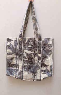 a black and white palm tree print tote bag hanging from a hook on a wall