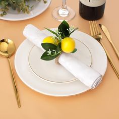 a table set with white plates, silverware and lemons