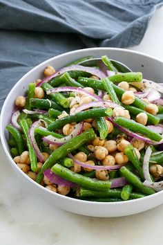 a white bowl filled with green beans and red onions on top of a table next to a blue towel