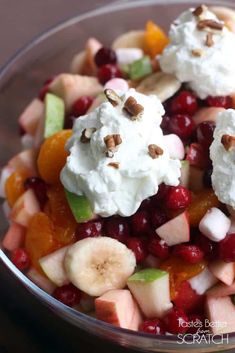 fruit salad with whipped cream and nuts in a glass bowl on top of a wooden table