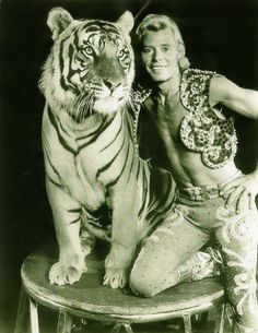 a man posing with a tiger on top of a stool