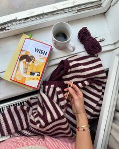 a woman is knitting on the window sill with her book and cup of coffee