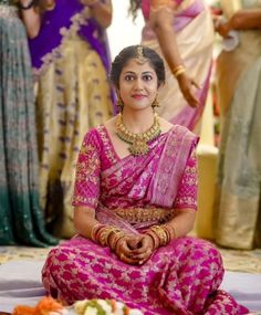 a woman in a pink sari sitting on the ground with other women around her